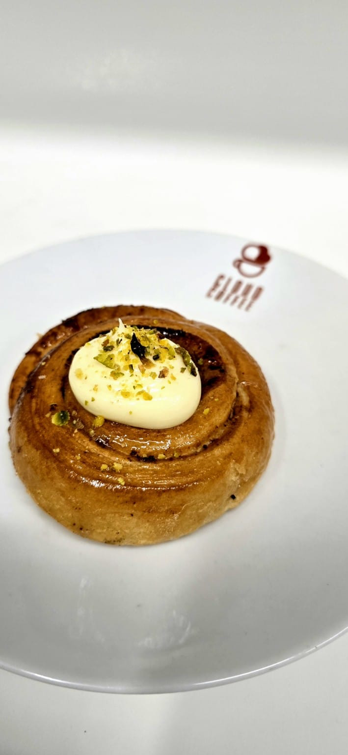 Honey glazed cinnamon roll topped with vanilla cream and pistachio crumble