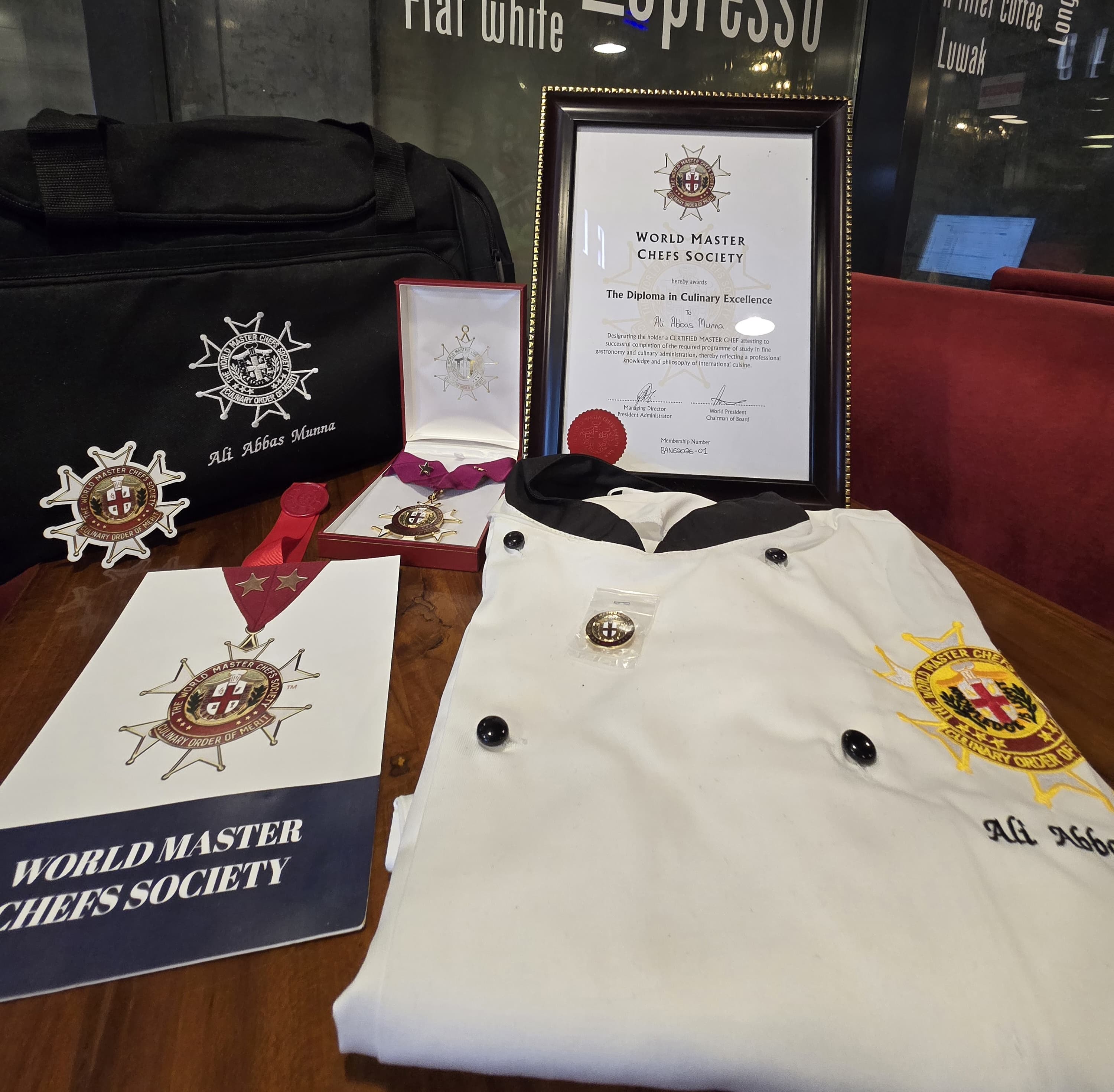 Chef Munna's World Master Chefs Society diploma, medal, chef coat, and credential materials arranged together on a table
