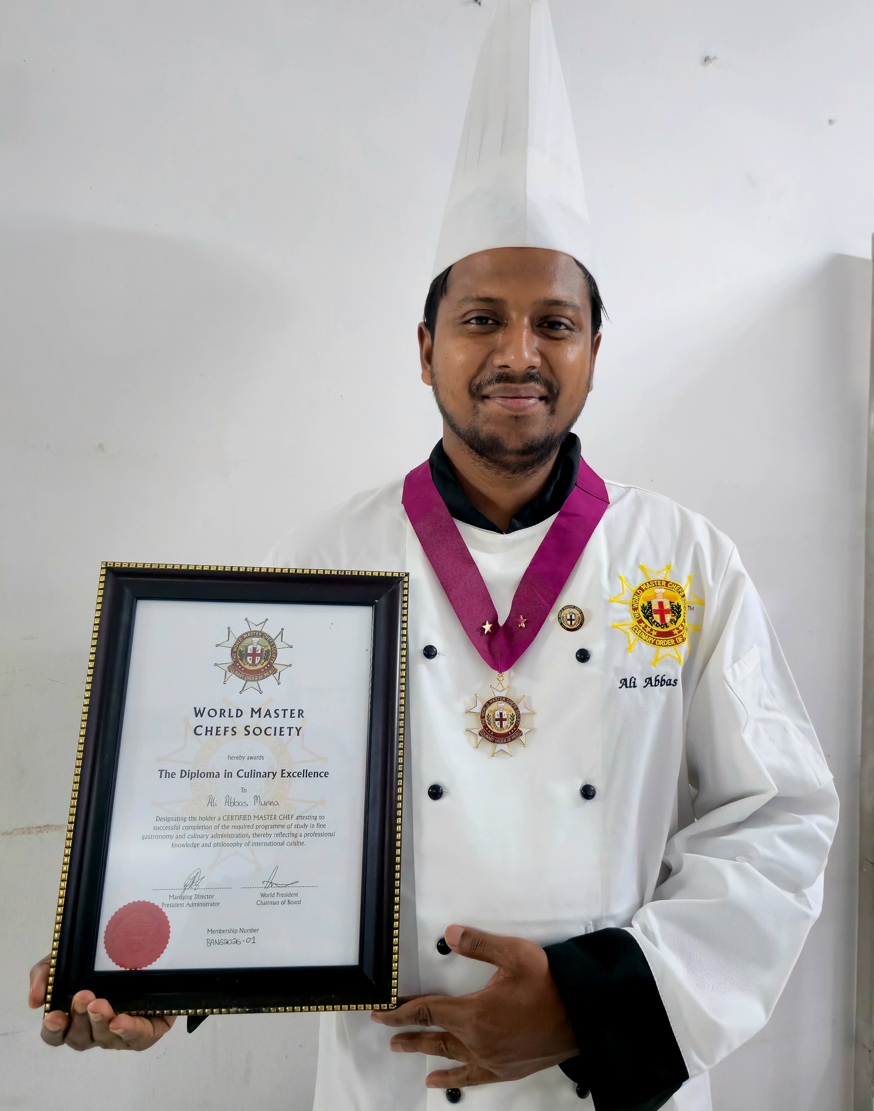 Chef Munna in full chef uniform holding his World Master Chefs Society diploma and wearing the medal